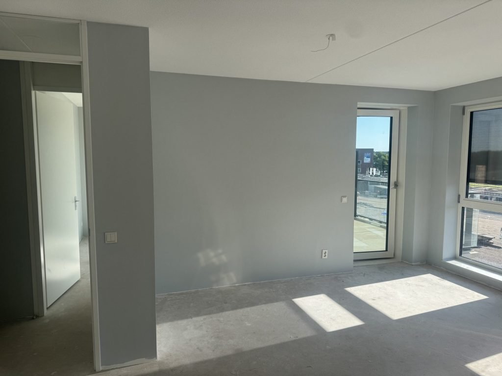 Appartement met lichtgrijze wanden, een balkondeur en een betonvloer vlak na het behangen