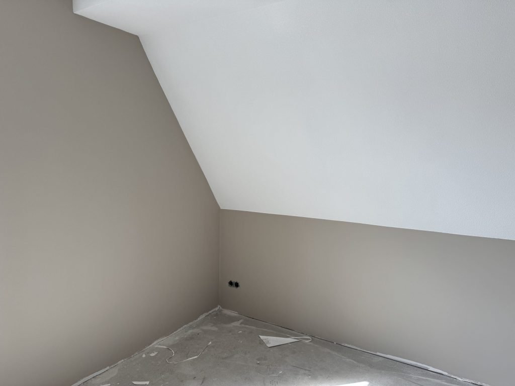 Zolderkamer met een schuine wand en beige gesausd vlies onder een wit plafond