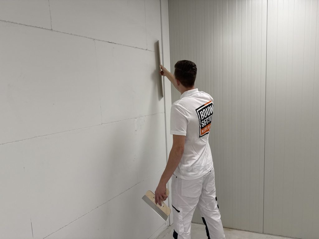 Vakman van Bouwsector Nederland zet een kale wand vlak met een spaan voordat het nieuwe vlies erop gaat